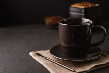 A black coffee Cup, metal jar of roasted coffee beans on a dark concrete table