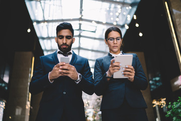 Ethnic clerks checking information with gadgets in hall