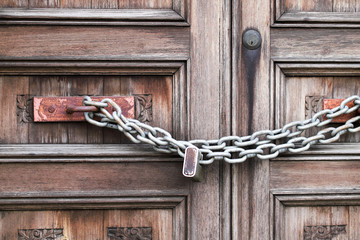 A double wooden door chained closed. Closeup of old wooden door with closed padlock on a chain. A chain of silver color with closed padlock on an old gate