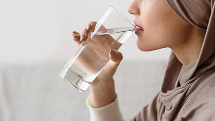 Islamic woman in hijab drinking clear water, holding glass in hand