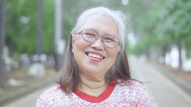 Slow motion of happy old woman smiling at the camera while standing in the park