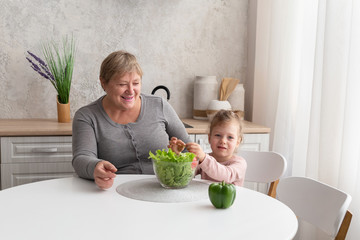 Grandmother and granddaughter prepare salad together in the kitchen. Happy family cooking healthy food