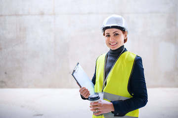 A woman engineer standing against concrete wall on construction site.