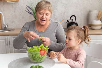 Happy grandmother and granddaughter prepare salad together in the kitchen. Family cooking healthy...
