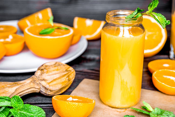 Cut oranges with juice in bottle and mint on kitchen background