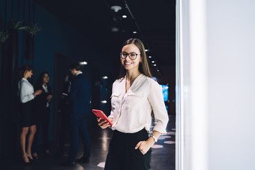 Happy confident businesswoman using smartphone in contemporary office building