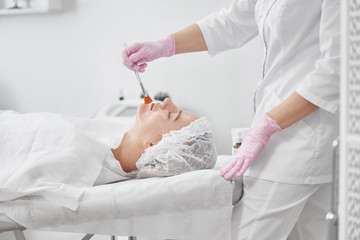 Professional beautician in salon provides comprehensive facial skin care for young woman. Pore cleansing procedures, all-season peeling, firming anti-aging mask