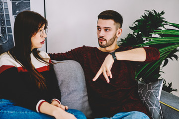 Caucasian couple in love sitting on comfort couch and making argue about solving problem in marriage, young friends discussing details while spending free time in flat with stylish decoration