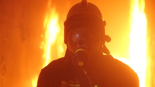 A firefighter looks at the camera against the background of the fire