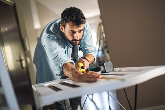 Man holding measuring tape in his hands and assembling a baby crib.
