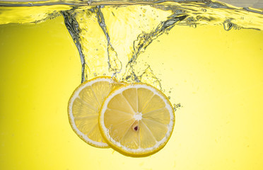 yellow lemon cut into slices drops under water on a yellow background