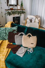 Set of multicolored knitted female bags with breast-bands are on a sofa in room.