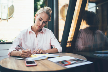 Concentrated woman writing in notebook in cafe