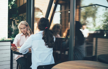 Woman at cafe with female friend using phone