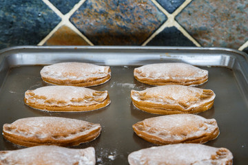 Christmas brown jam cookies on a pan in neat rows waiting for baking; raw cookie dough shaped half circles and filled with jam