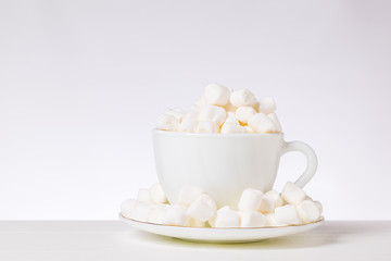 Small pieces of marshmallow in a white Cup and saucer on a white table.