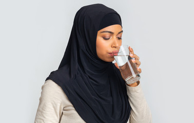 Black islamic girl in hijab drinking water from glass in studio