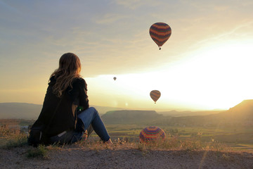 Woman looking at Air baloons flying at sunrise in Cappadocia
