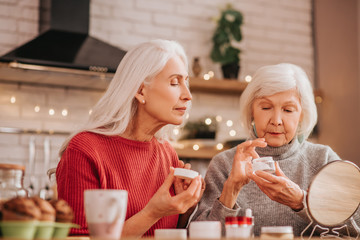 Two good-looking elderly women applying new cream