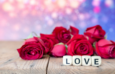 Love sign on wooden cubes and red roses flower on wooden table. Love and Valentine day concept.