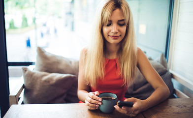 Young content woman using smartphone in cafe
