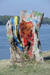 A rotten tree trunk on the riverbank. Someone has colored the log with different colors. There are also colored handprints. - 317034726