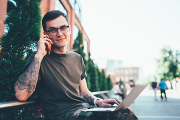 Cheerful young man using laptop and smartphone in street