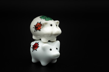 Two small white porcelain piggies, black background