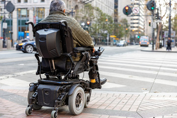 An elderly disabled person on an electric wheelchair on a city street in front of a pedestrian crossing. The concept of modern technology for people with disabilities.