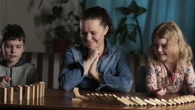 Family fun to spend leisure time playing with wooden sticks. Table games for the whole family. Mother with daughter and son falling wooden dominoes.Family games in your home. Fun and laughter.