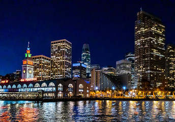 Fototapeta na wymiar Panoramic view of the port of San Francisco, illuminated at night, against the backdrop of impressive skyscrapers with light and reflection in the water, view from the side of the San Francisco Bay.