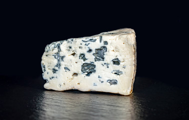 a piece of cheese with blue mould on a black background closeup