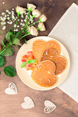 Homemade heart shaped pancakes with fruit chutney salad and honey on a beige plate on a wooden table. Rustic style breakfast or brunch for Valentine's Day. Top view, vertical orientation