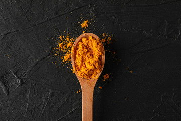Wooden spoon with turmeric powder on black background, top view