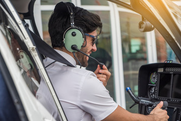 Pilot with headset starting the controls in the private helicopter. Helicopter pilot sitting in the cockpit. © supAVADEE BUTRADEE
