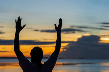 Silhouette of a happy african guy with hands up during sunset by the ocean on the island of Zanzibar, Tanzania, East Africa