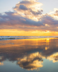 Fototapeta na wymiar Beautiful warm golden sunlit clouds during sunset perfectly reflecting in the sand on a beach. Fire Island National Seashore - New York