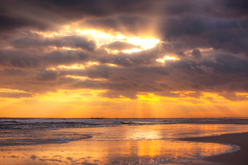 Golden beams of sunlight (God rays) breaking through dark stormy clouds over a beach. Fire Island New York. 