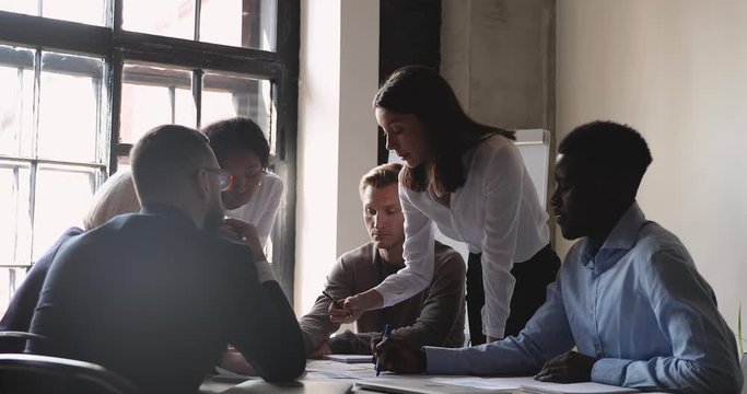Serious female manager and diverse team analyze paperwork at meeting