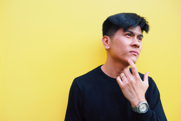 Young Asian man touching his face with facial skin problem about acne moles and pores isolated on yellow background. Feeling worried about his look. Men health and aesthetics concept