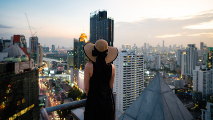 Beautiful woman standing on the rooftop of a skyscraper. Back view of young woman in hat on the...