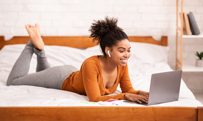 African American Girl Using Laptop Studying Online Lying On Bed