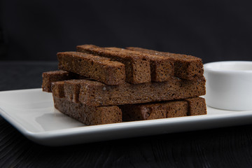 Crackers with garlic from black bread in oil on a wooden black background.