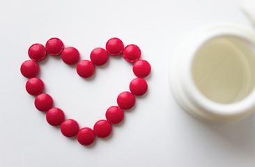 The red tablets are arranged in the shape of a heart. Red heart pills with a plastic jar. The concept of a healthy heart.