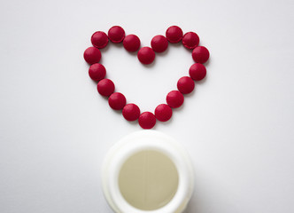 The red tablets are arranged in the shape of a heart. Red heart pills with a plastic jar. The concept of a healthy heart.