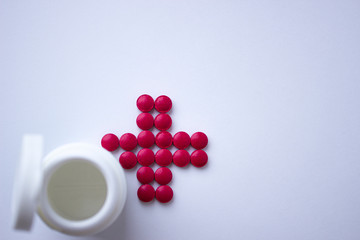 The tablets are arranged in the shape of a cross. Red tablets with a plastic jar. The concept of health. Help with recovery. Red cross.