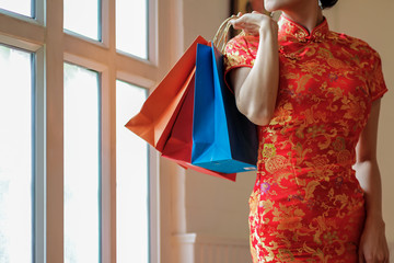 A woman wearing a red cheongsam on Chinese New Year is carrying a colorful paper bag after shopping for cheap goods at a discounted price during Chinese New Year as a gift for lovers and families.