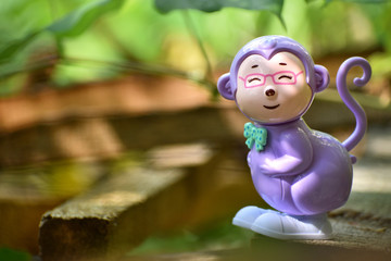 A jumping monkey toy standing on the woods with greenish blurred background.