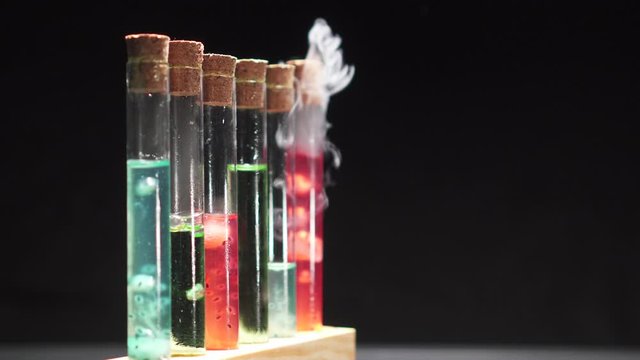 Glass test tubes with boiling multi-colored liquid on a black background, close-up. Scientific research concept.