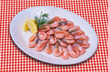 Plateful of cooked shrimps with lemon slice on checked tablecloth